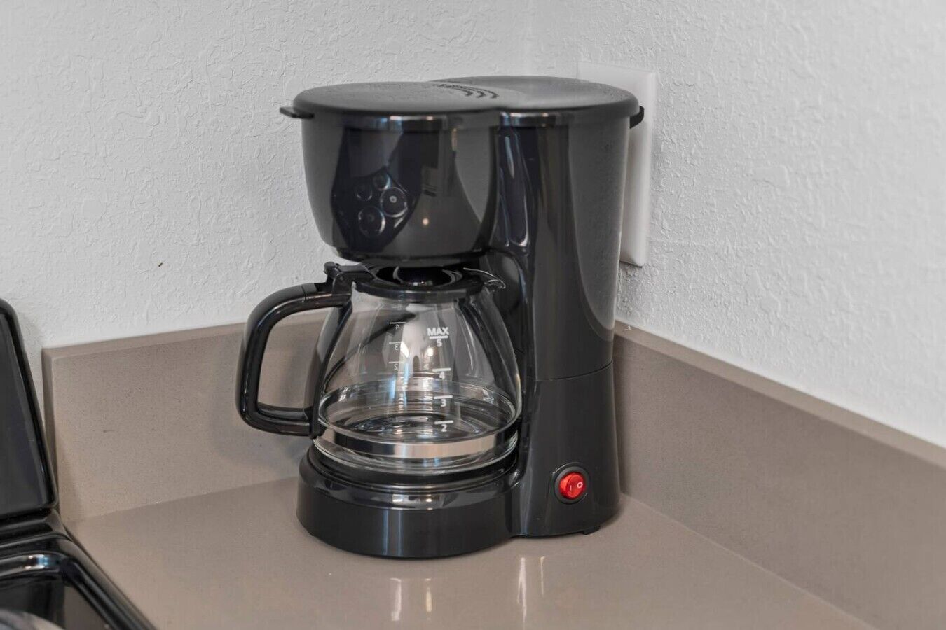Une machine à café noire avec une verseuse en verre, posée sur un plan de travail.