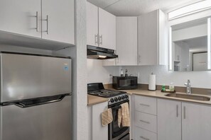 Eine kompakte Küche mit einem Edelstahl-Kühlschrank, einem Herd, einer Mikrowelle und einem Spülbecken mit Wasserhahn.