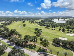 Een golfbaan met zandbunkers, bomen en een heldere lucht.