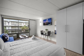 A modern hotel room with a bed, a seating area with a table and chairs, a TV mounted on the wall, and a wardrobe. - Bright Disney Suite + Pool & Parking | Orl (Kissimmee)