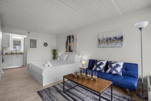 A modern hotel room with a bed, a blue sofa, a coffee table, and a painting on the wall. - Bright Disney Suite + Pool & Parking | Orl (Kissimmee)