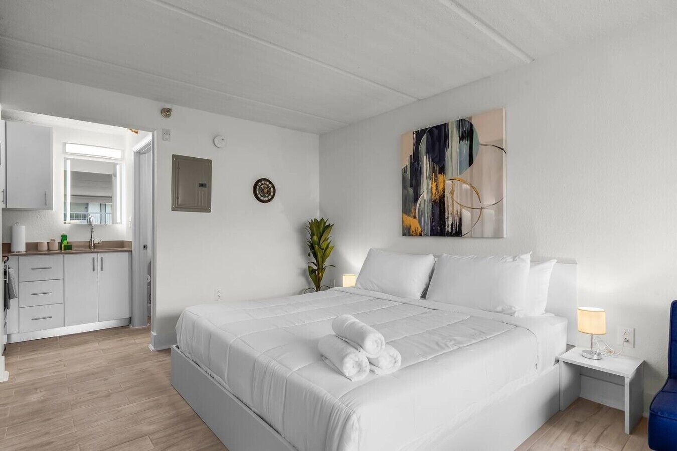 Een hotelkamer met een groot bed, een nachtkastje met een lamp, een wandklok en een schilderij.