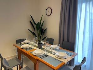 A dining table set for four with chairs, a clock on the wall, and a plant on the table.