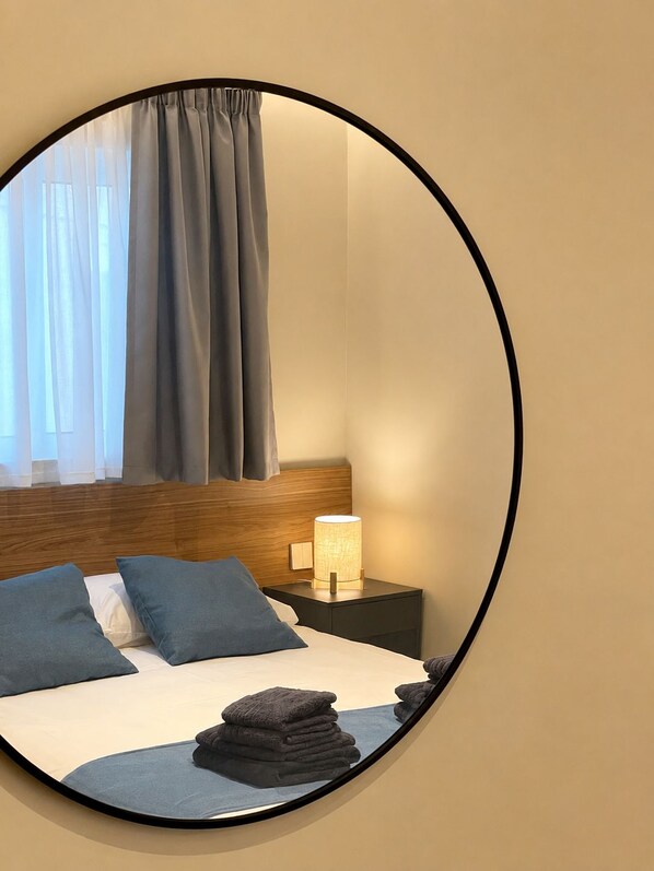 A bedroom with a bed, pillows, a nightstand, a lamp, and a mirror.