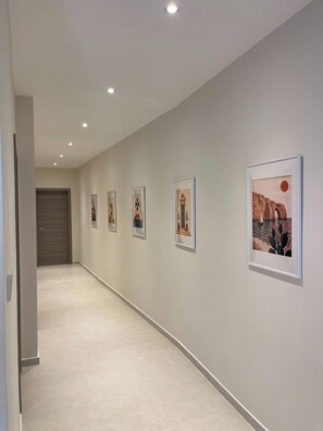 A hallway with a series of framed artworks on the wall and a door at the end. - Modern & Stylish 3BR Apartment in Central Malta (L-Imsida)