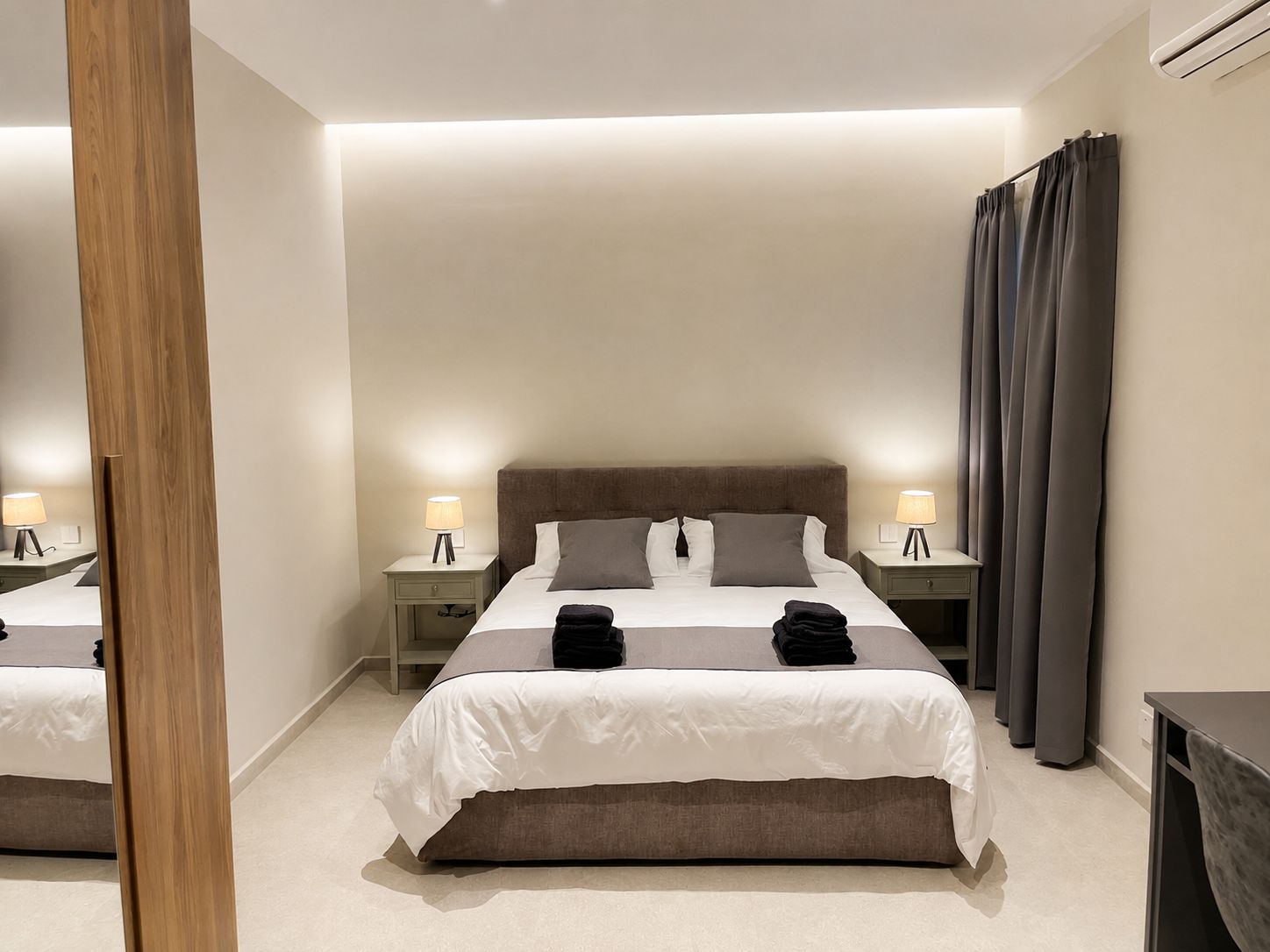 Ein Hotelzimmer mit einem großen Bett, zwei Nachttischen mit Lampen, einem Spiegel und einem Vorhang.