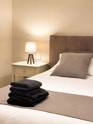 A neatly made bed with a pillow, a bedside lamp, and a stack of folded towels. - Modern & Stylish 3BR Apartment in Central Malta (L-Imsida)