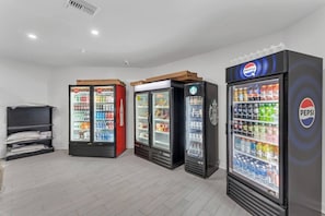 Varias máquinas expendedoras de bebidas con la marca Pepsi y Coca-Cola, un depósito con sábanas dobladas y una pared blanca lisa.