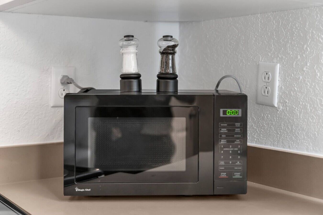Eine Mikrowelle mit digitaler Anzeige, Bedienfeld und zwei Glasbehältern darauf.