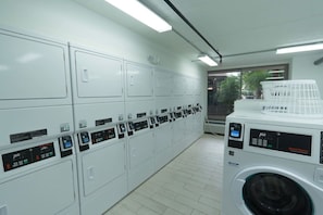 A laundry facility with multiple washing machines and dryers, a tiled floor, and a window providing natural light. - Cozy Disney Retreat + Parking Included | Orl (Kissimmee)