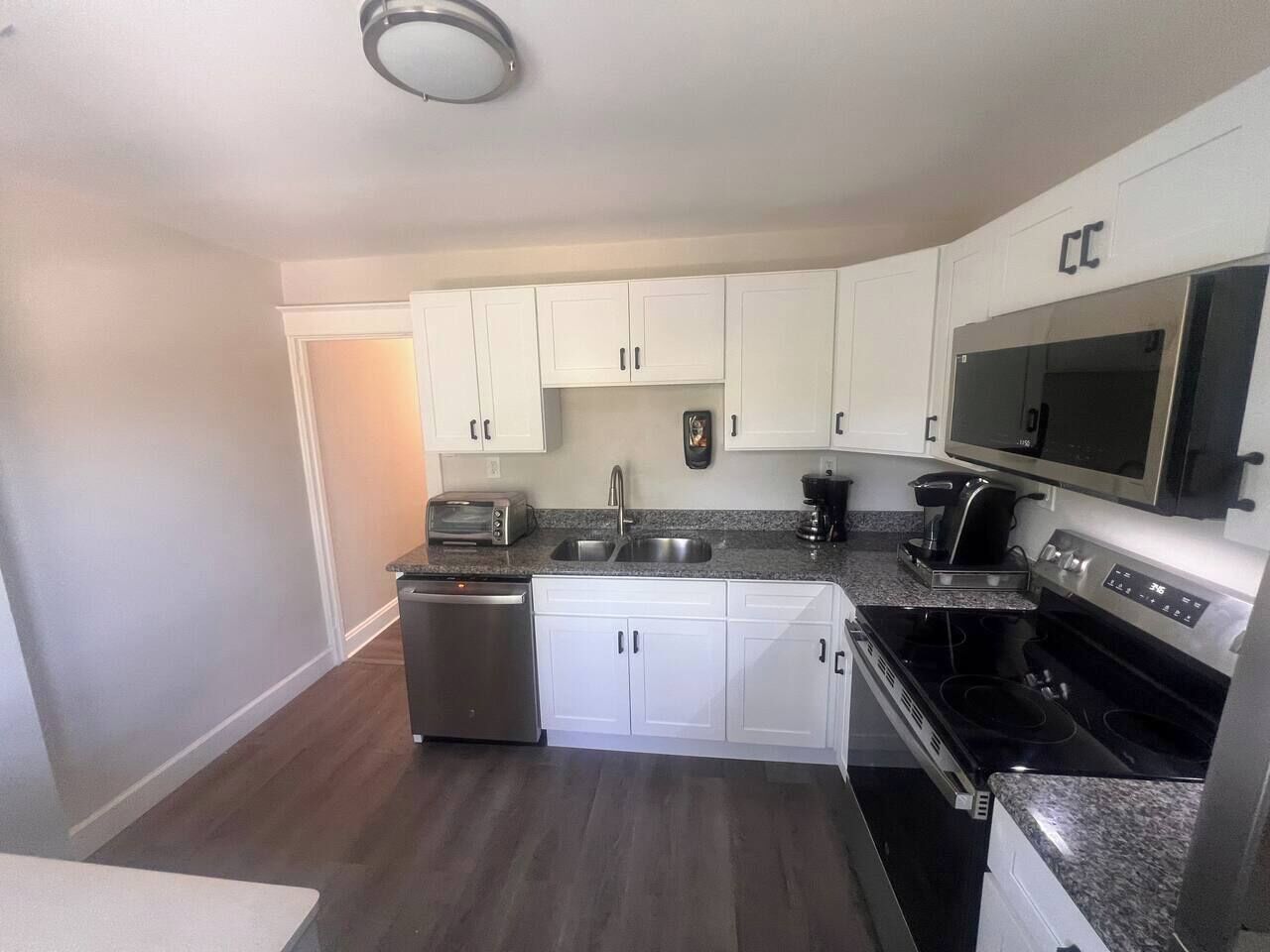 A compact kitchen with white cabinets, a stainless steel dishwasher, a microwave, and a stove.