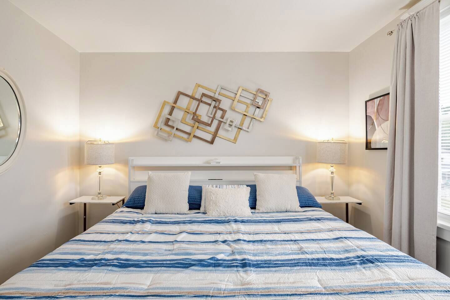 A hotel room with a bed, two bedside tables, a wall-mounted artwork, and a window with curtains.
