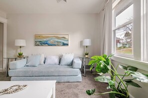 A living room with a sofa, two side tables with lamps, a painting on the wall, and a large window with curtains. - Overlook at Wyoming avenue (Enola)