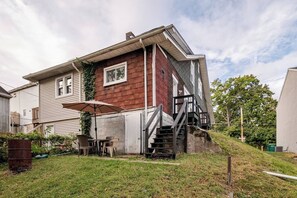 Une maison à deux étages dotée d’un patio couvert, d’un escalier menant à l’étage supérieur et d’un petit jardin à l’avant.