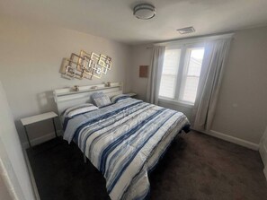 Une chambre à coucher comprenant un lit, des tables de chevet, une fenêtre avec des rideaux et un luminaire fixé au mur.
