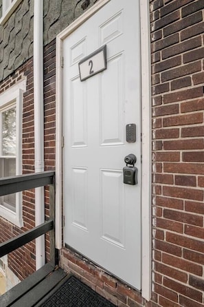 A white door with a number plate, a keypad lock, and a small window to the left.
