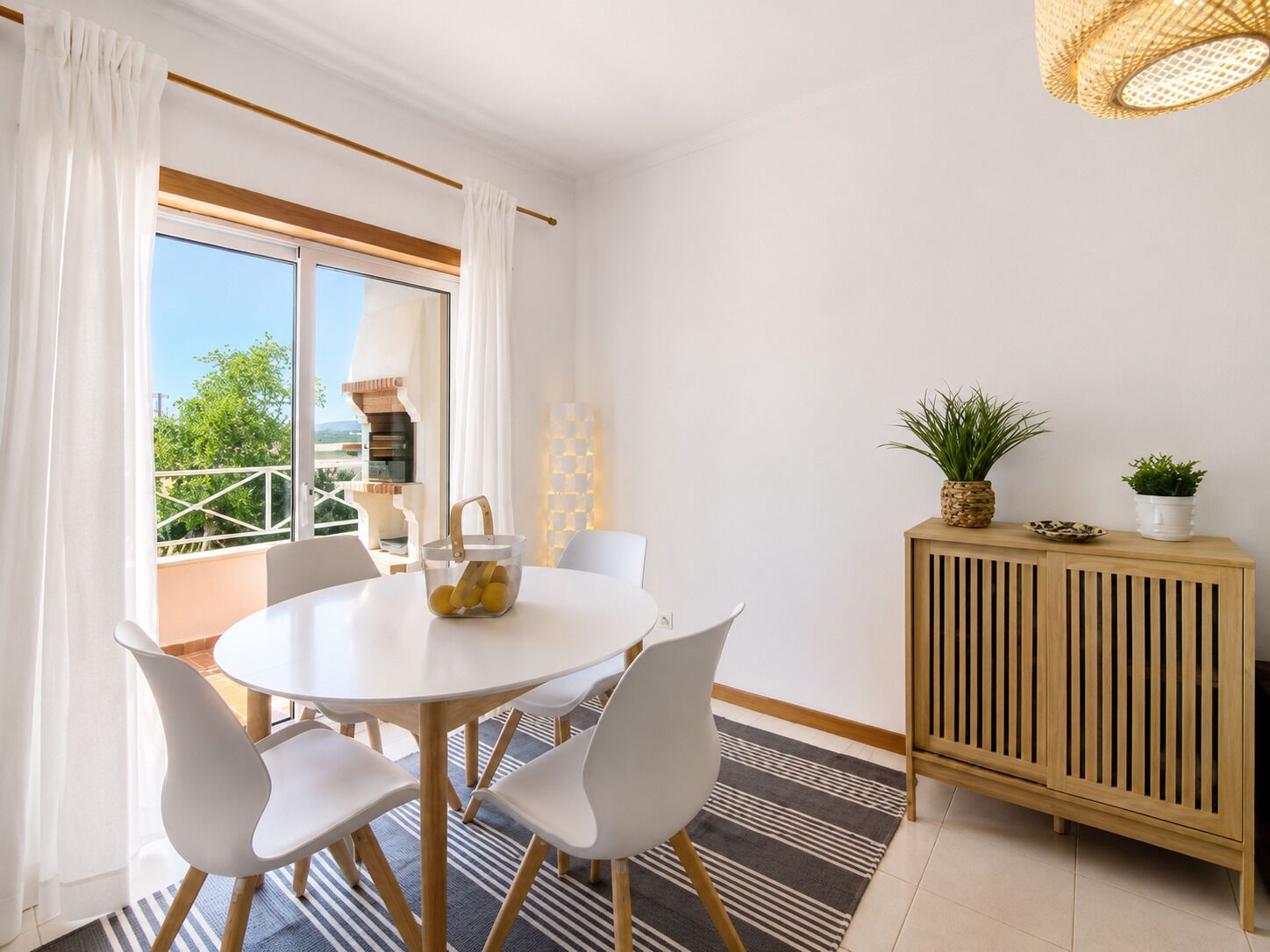A modern dining area with a round table, white chairs, a wooden cabinet, and a view of the outdoors.
