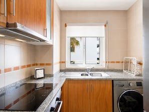 A kitchen with a built-in oven, a dishwasher, and a window with a view of a balcony. - AE Flat Falésia - 1-Bedroom Apartment in Praia da Falésia with Air Conditioning and Wi-Fi (Albufeira)