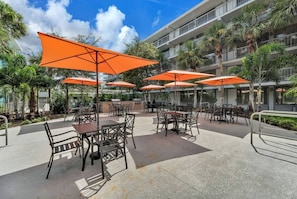 Un espace extérieur aménagé en terrasse, avec des tables et des chaises, entouré de parasols orange, et un bâtiment avec des balcons en arrière-plan.