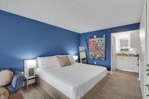 A bedroom with a bed, bedside tables, a nightstand, a desk, a chair, a painting, and a view of a bathroom. - Modern Disney Escape + Free Parking | Orl (Kissimmee)