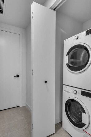 A laundry room with a closed door, a stacked washer and dryer, and a tiled floor. - Stunning Skyline & Bay View Luxury Apartment (Miami)