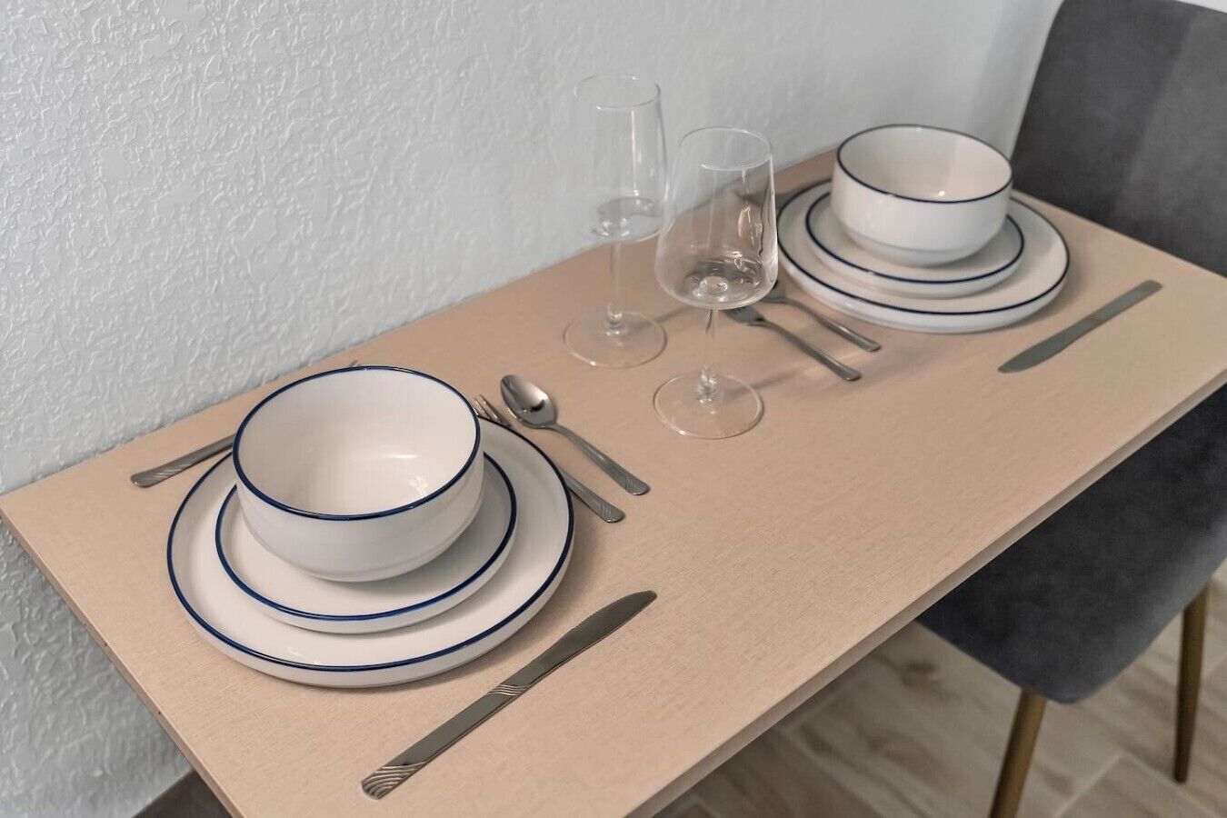 Una mesa de comedor dispuesta con cuencos y platos blancos, un cuchillo, una cuchara y dos copas de vino.