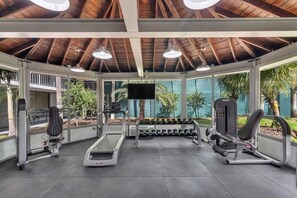 Een overdekte gymzaal met loopbanden, gewichten en krachtapparaten, met grote ramen en een houten plafond.