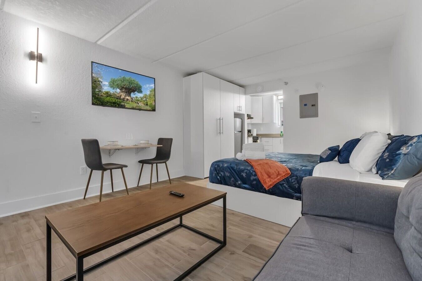 Een moderne, compacte leefruimte met een bed, een slaapbank, een eethoek en een kitchenette.
