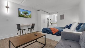 A modern, compact living space with a bed, a sofa, a dining area, and a kitchenette.