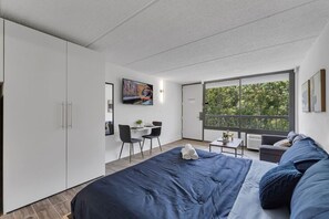 Un dormitorio moderno con una cama grande, un escritorio y un balcón con vistas a árboles.