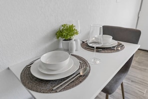 A dining table set with white plates, bowls, and cutlery, accompanied by a glass of wine and a small potted plant. - Dream Studio 7 Min to Disney + Gym & Parking I Orl (Kissimmee)