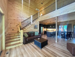 Amplia sala de estar con una escalera de madera, un sofá de cuero, una mesa de centro y una cocina al fondo.