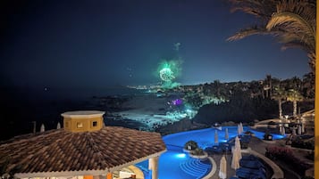 A resort with a pool, palm trees, and a view of the ocean at night.