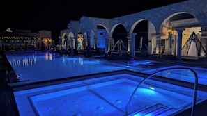 Ein Poolbereich bei Nacht mit Steingewölben und blauer Beleuchtung.