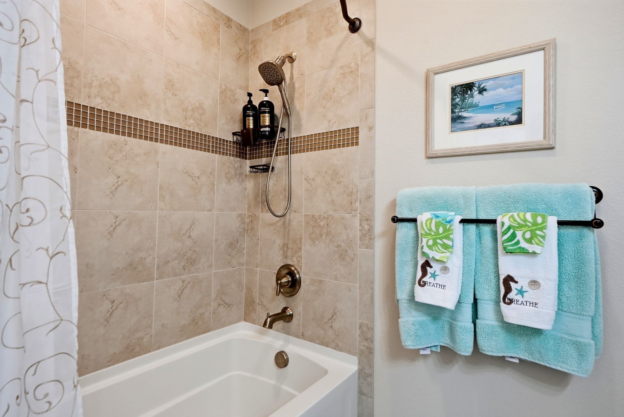 A bathroom with a bathtub, shower, and two towels with sea creature designs.