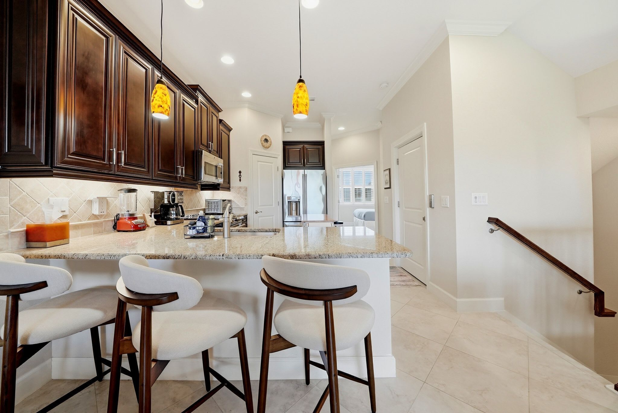 A modern kitchen with dark wood cabinets, a granite countertop, and a central island with bar stools.