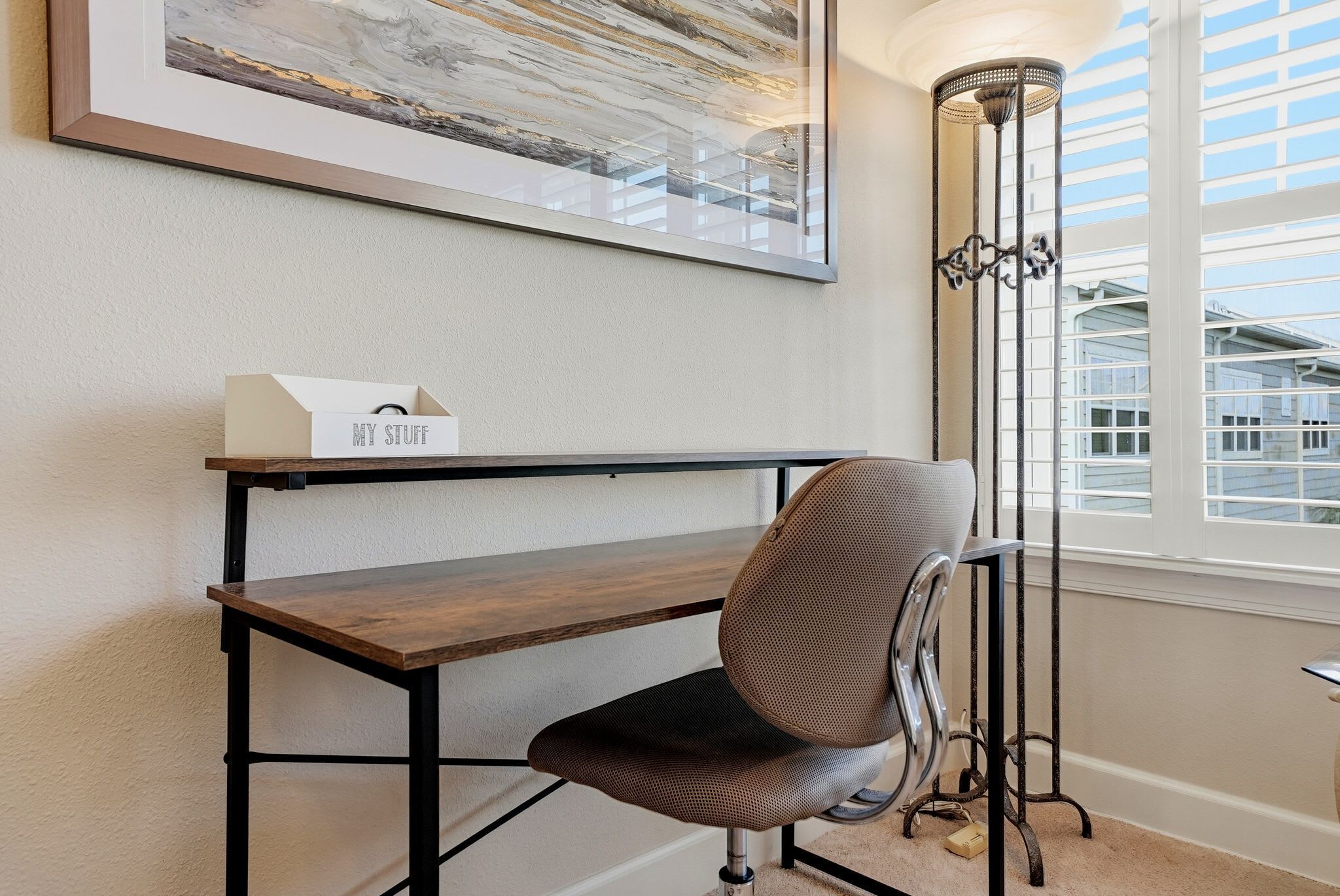 A workspace with a desk, chair, and a framed abstract painting on the wall.