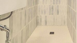 Un baño con lavamanos blanco, grifo dorado y zona de ducha con paredes y suelo de baldosas.