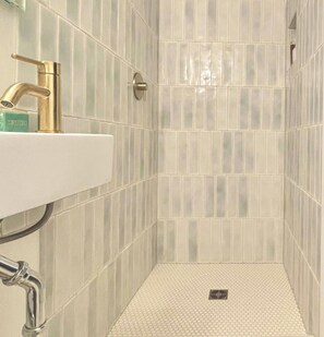 Un bagno con lavandino bianco, rubinetteria dorata e zona doccia con pareti e pavimento piastrellati.