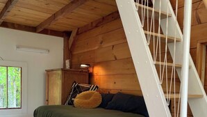 Un dormitorio con una cama litera de madera, una mesita de noche con lámpara y una ventana que da a vista de árboles.