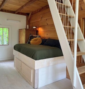 Una camera da letto con un letto a castello in legno, un comodino con una lampada e una finestra vista alberi.