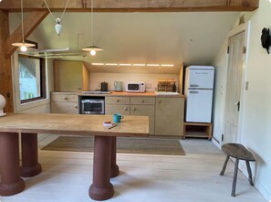 Una cucina compatta con un tavolo di legno, un frigorifero, un forno a microonde e una macchina da caffè.