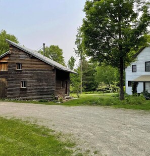 Un edificio in legno rustico con tetto spiovente e vialetto sterrato che conduce a una zona verde.