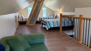 Een slaapkamer in een loft met een schuine wand, twee bedden, een trap en een groene bank.