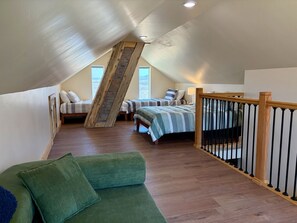 Quarto no estilo loft com teto inclinado, duas camas, escada e um sofá verde.