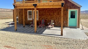 Een houten chalet met twee verdiepingen, een balkon, een groene deur en buitenmeubilair.