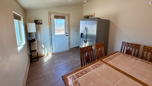 Een eetgedeelte met een tafel, stoelen, een koelkast en een deur naar een andere kamer.