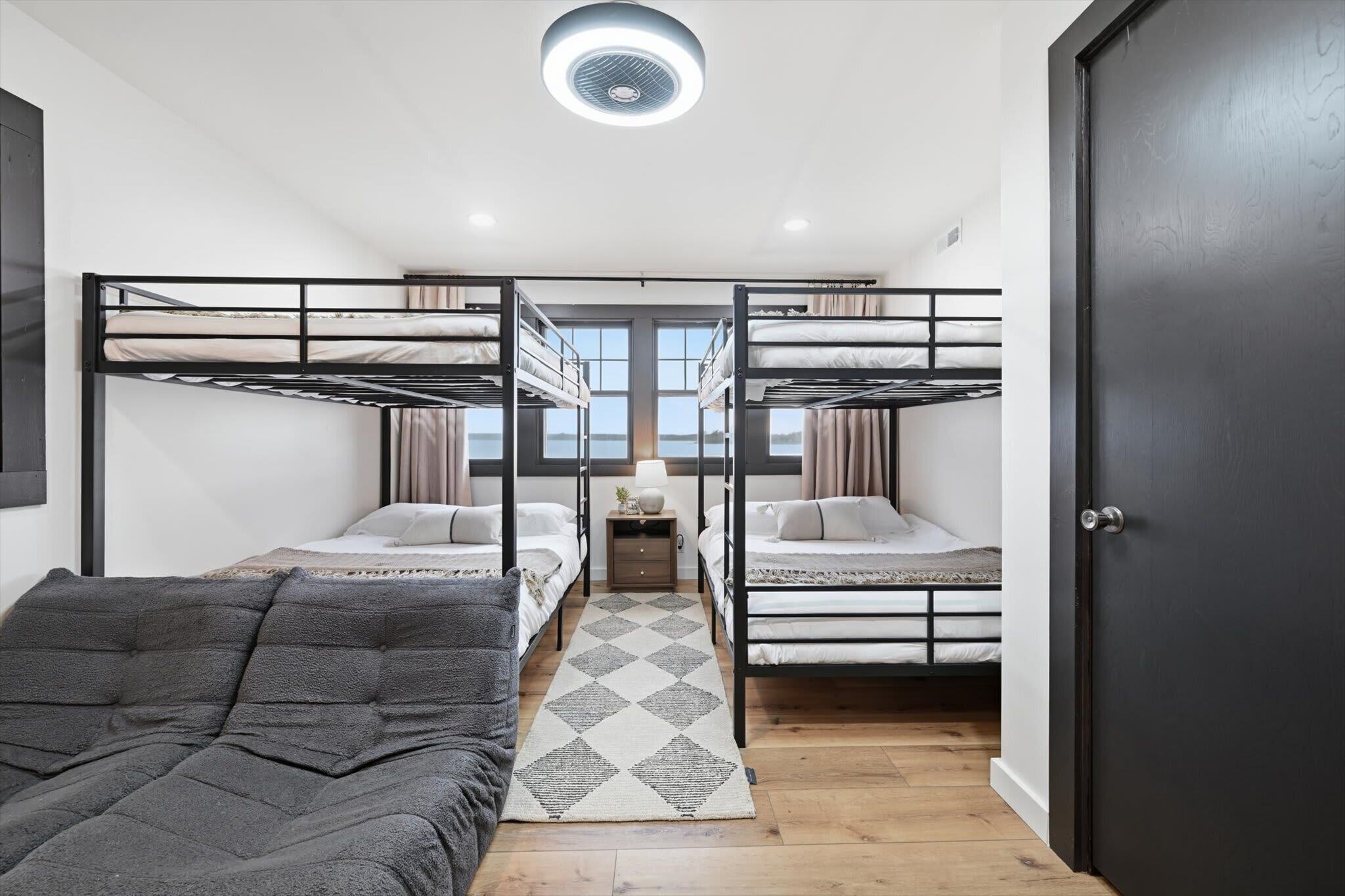 Une chambre avec des lits superposés, une petite table avec une lampe et une vue dégagée grâce à de grandes fenêtres.