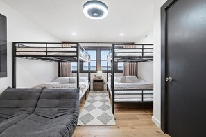 A room with bunk beds, a small table with a lamp, and a view through large windows.