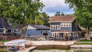Une propriété située au bord de l’eau, dotée d’un quai, d’un espace salon couvert et d’une maison à deux étages avec un balcon.
